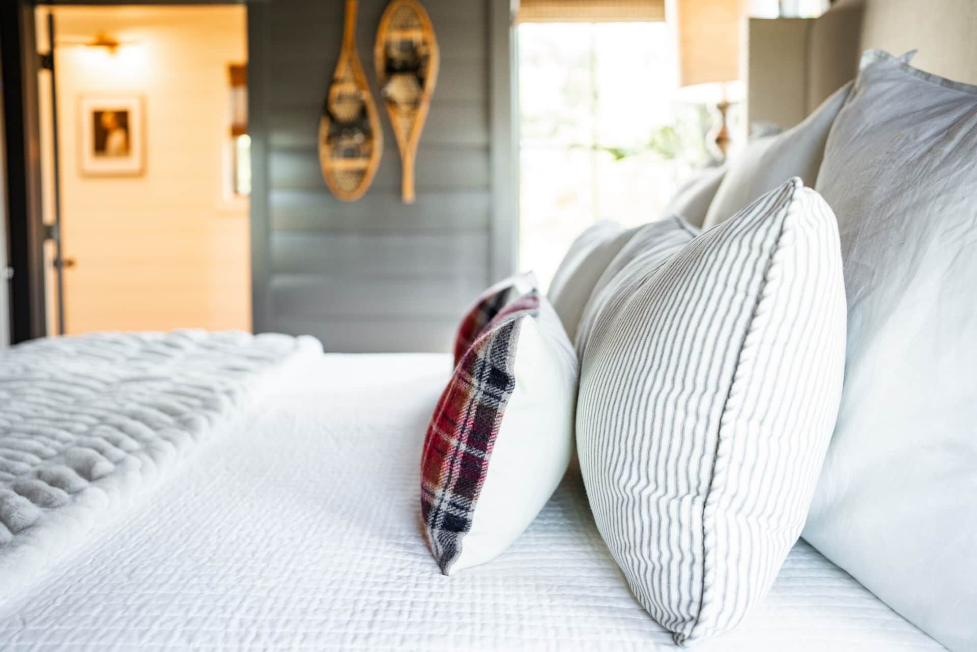 A neatly made bed with white bedding and a plaid throw pillow.