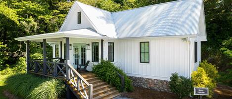 A white house with a porch, a stone foundation, and a sign indicating it is a boat house.