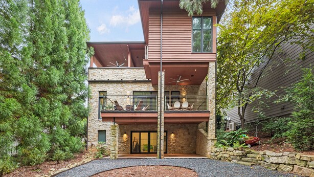 A modern two-story house with a stone facade, a balcony with outdoor seating, and a well-maintained garden. - The Red House in Serenbe w/ Golf Cart (Palmetto)