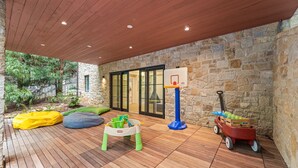 An outdoor patio with a wooden deck, stone walls, a basketball hoop, and children's play equipment. - The Red House in Serenbe w/ Golf Cart (Palmetto)