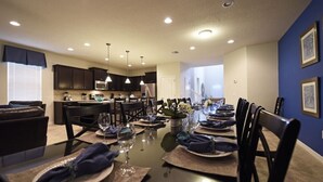 Uma sala de jantar com uma mesa comprida posta para refeição, rodeada por cadeiras escuras.