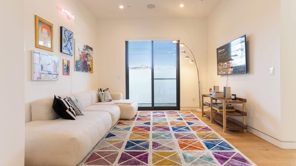 A living room with a sofa, a colorful rug, a TV, and artwork on the wall. - Luxe Weho Villa, Walk to Melrose Ave, Pool + Hot Tub North Vista by Avantstay (Los Angeles)