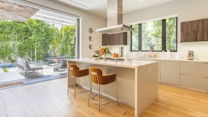 Una cocina moderna con una isla grande, taburetes de bar y vistas a un jardín a través de amplios ventanales.