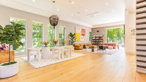 Amplia sala de estar con piso de madera, muebles blancos y ventanas grandes que dan a zonas verdes.