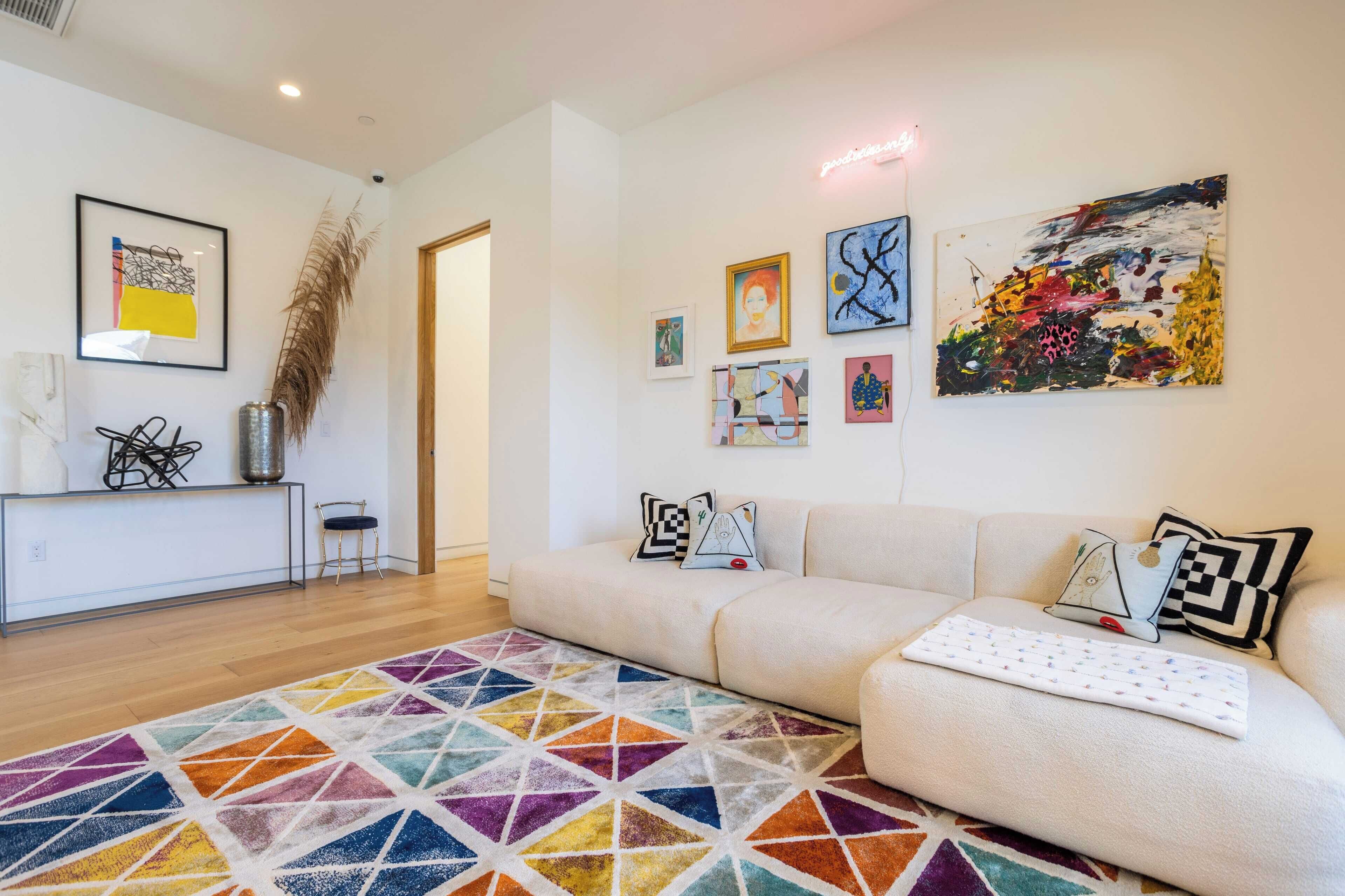 Un salon moderne avec un canapé, un tapis coloré et diverses œuvres d’art accrochées aux murs.