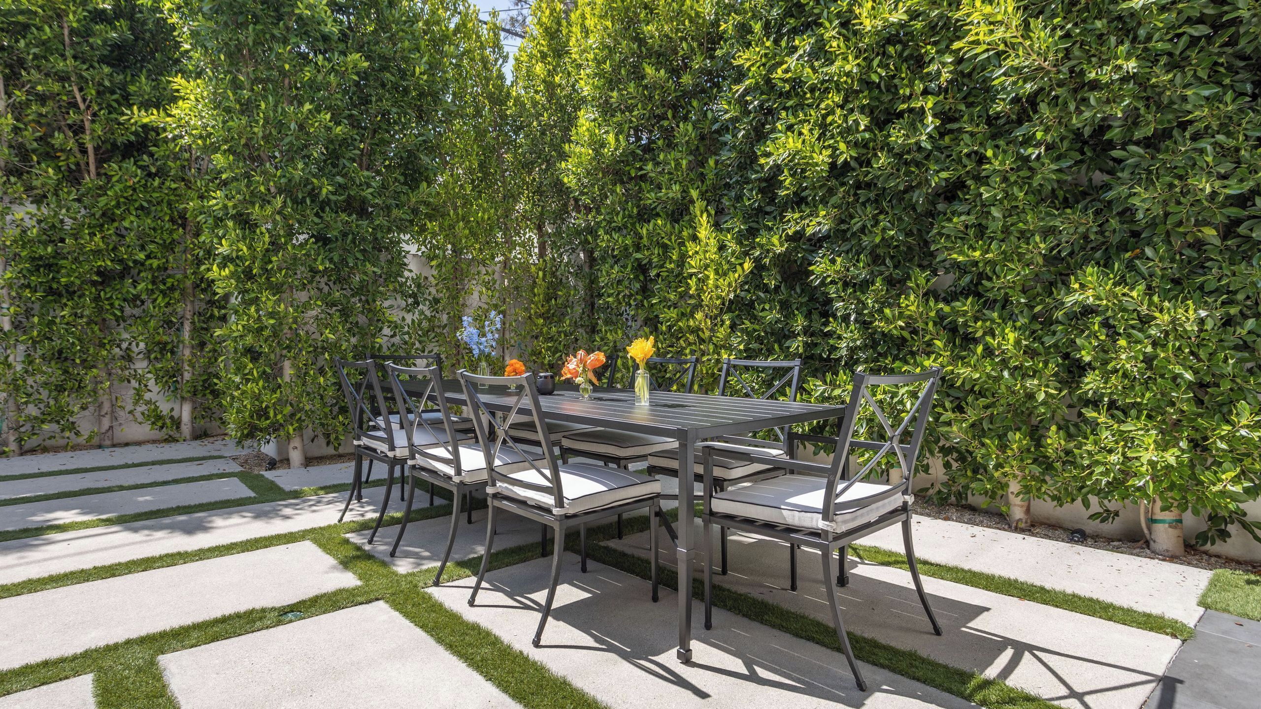 An outdoor patio with a rectangular table and chairs, surrounded by lush greenery.