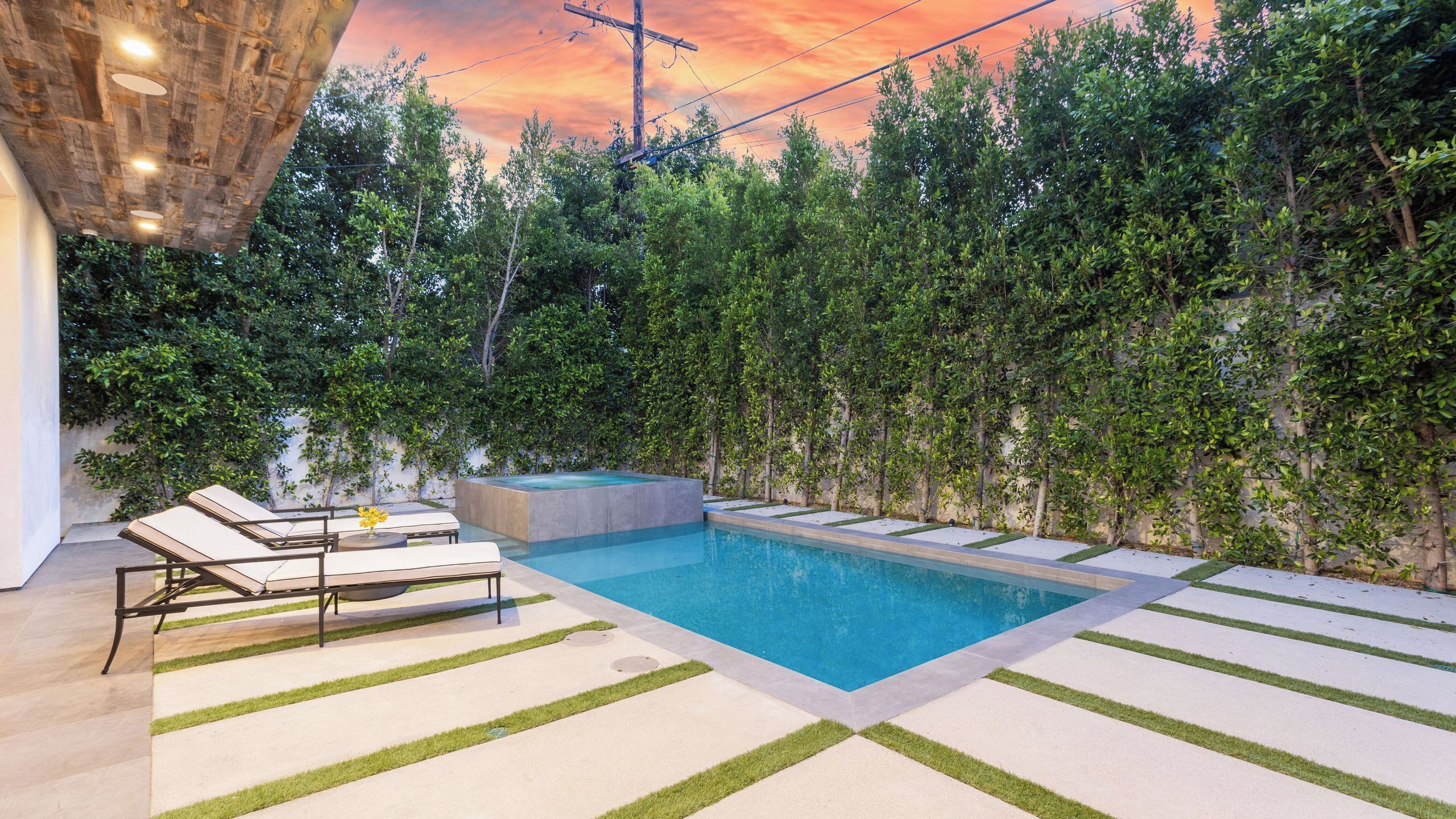 A modern outdoor pool area with lounge chairs, a hot tub, and a well-maintained garden.