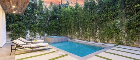 A modern outdoor pool area with lounge chairs, a hot tub, and a well-maintained garden.