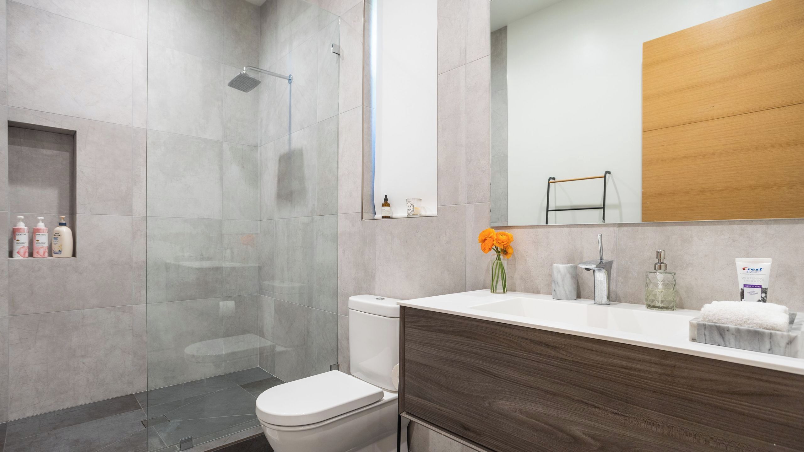 Un baño moderno con cabina de ducha de vidrio, inodoro blanco, tocador con lavamanos de mármol y espejo sobre el lavamanos.