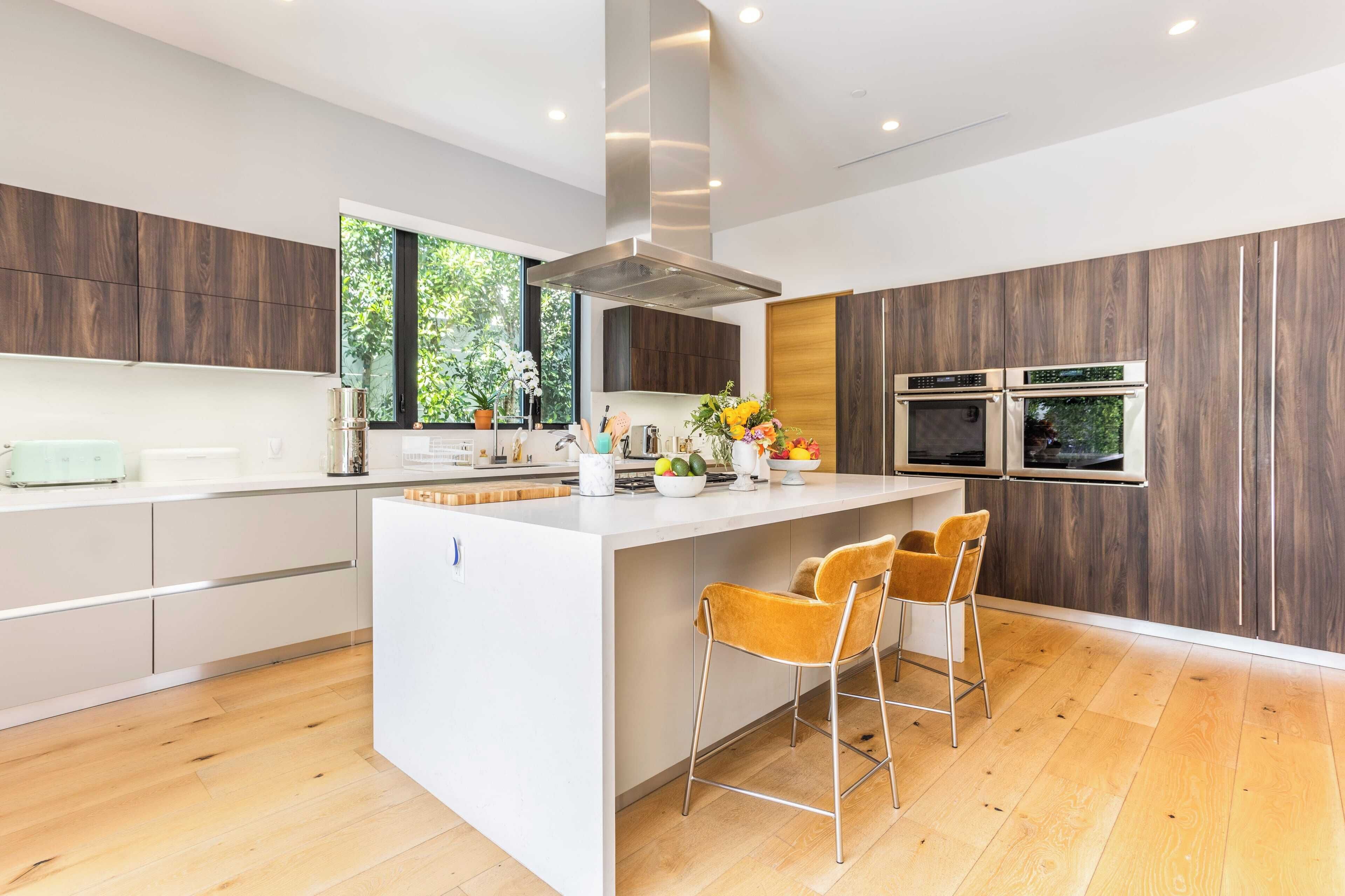 A modern kitchen with a central island, wooden cabinets, and a large window.