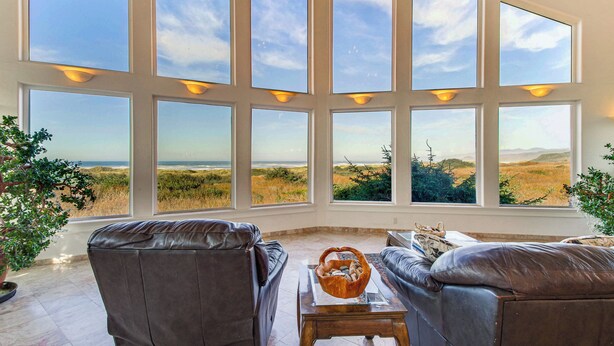 Ein Zimmer mit großen Fenstern und Blick auf eine grüne Landschaft. Zwei Ledersofas und ein kleiner Tisch mit einer dekorativen Schale sind vorhanden.