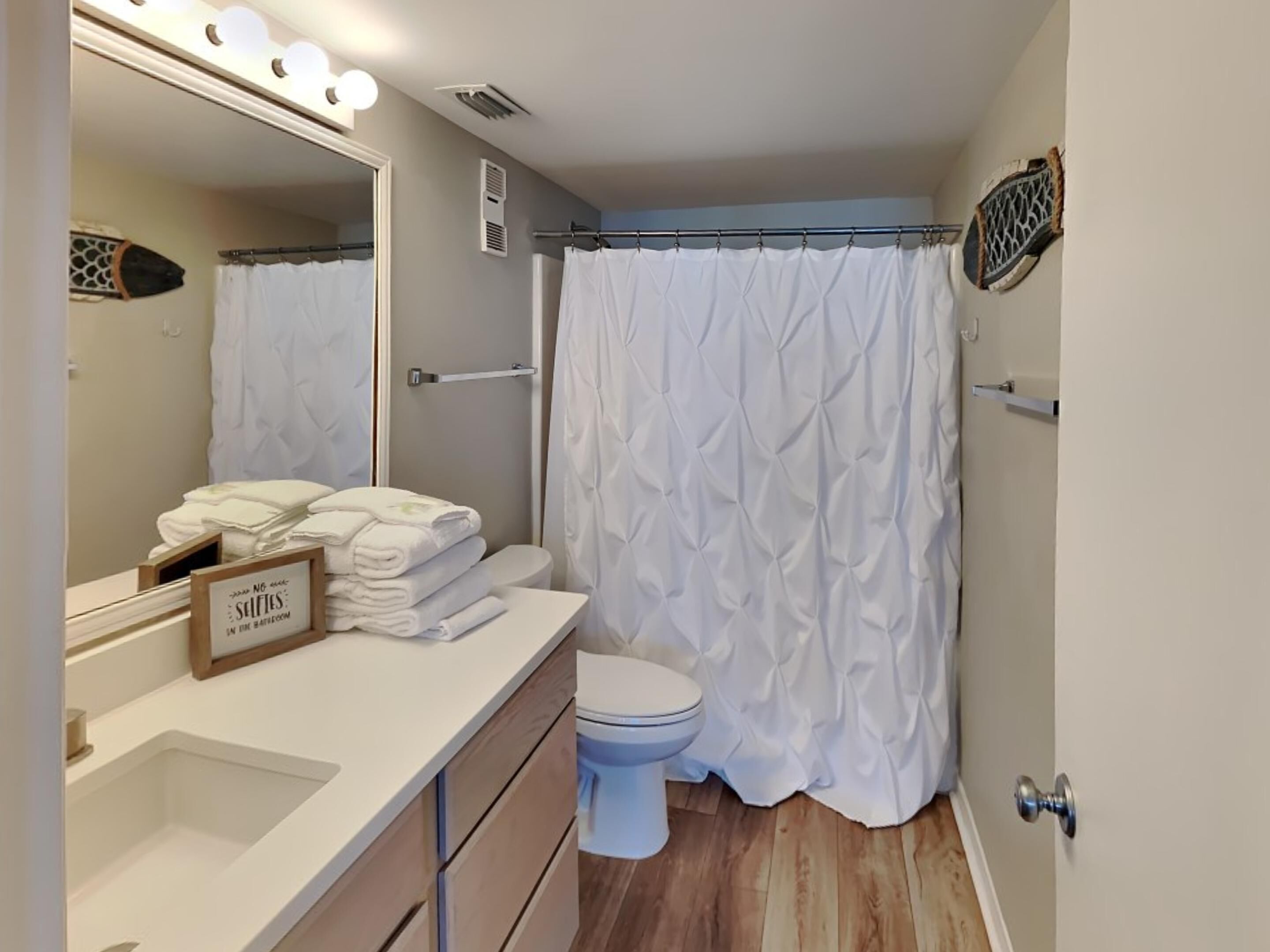Un bagno con un lavandino bianco, uno specchio, un portasciuga e una tenda da doccia.