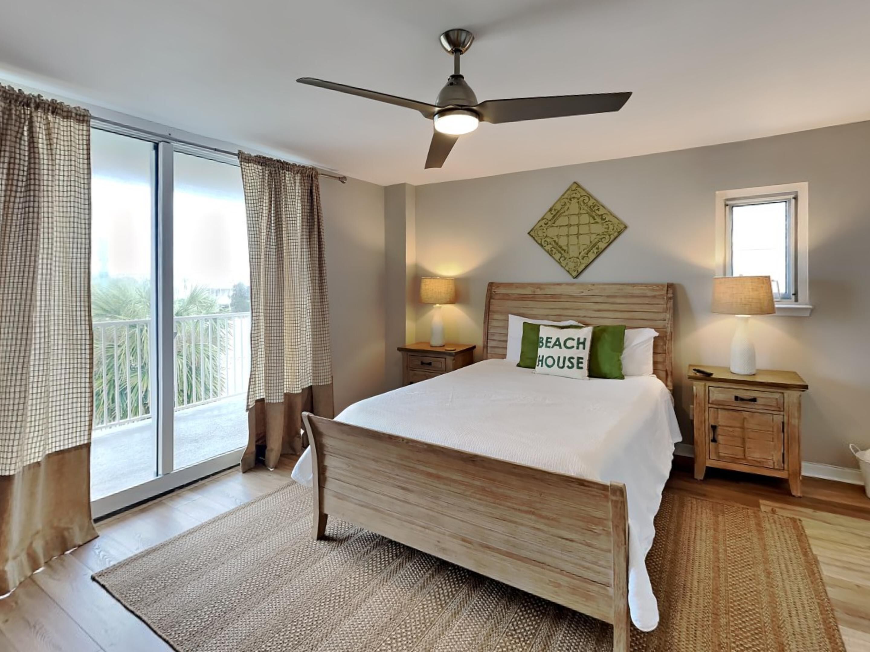 Une chambre à coucher comprenant un lit, un ventilateur de plafond, deux tables de chevet avec des lampes, une fenêtre avec des rideaux et une vue sur l’extérieur.