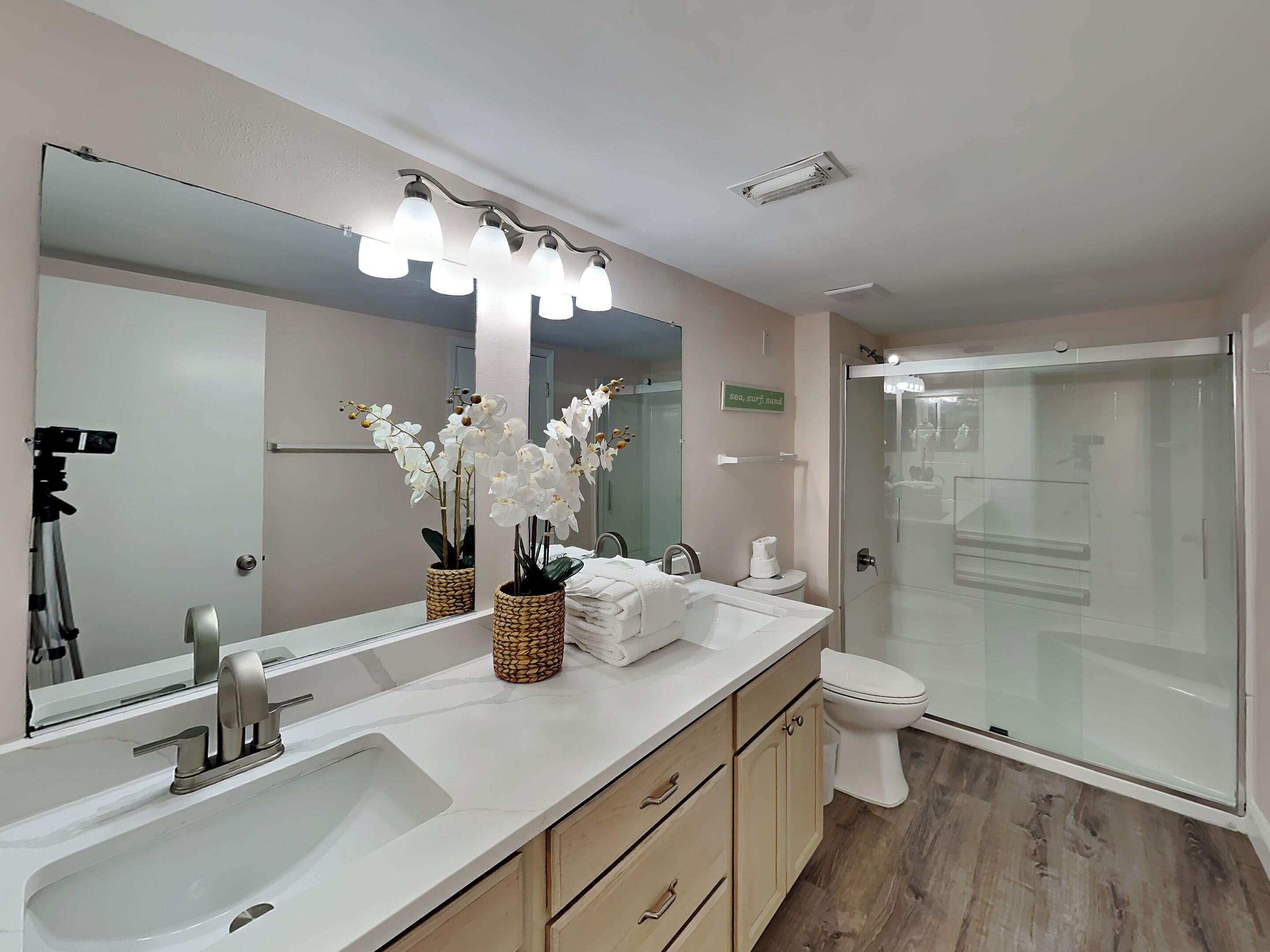 A modern bathroom with a large mirror, white sink, and a glass shower enclosure.