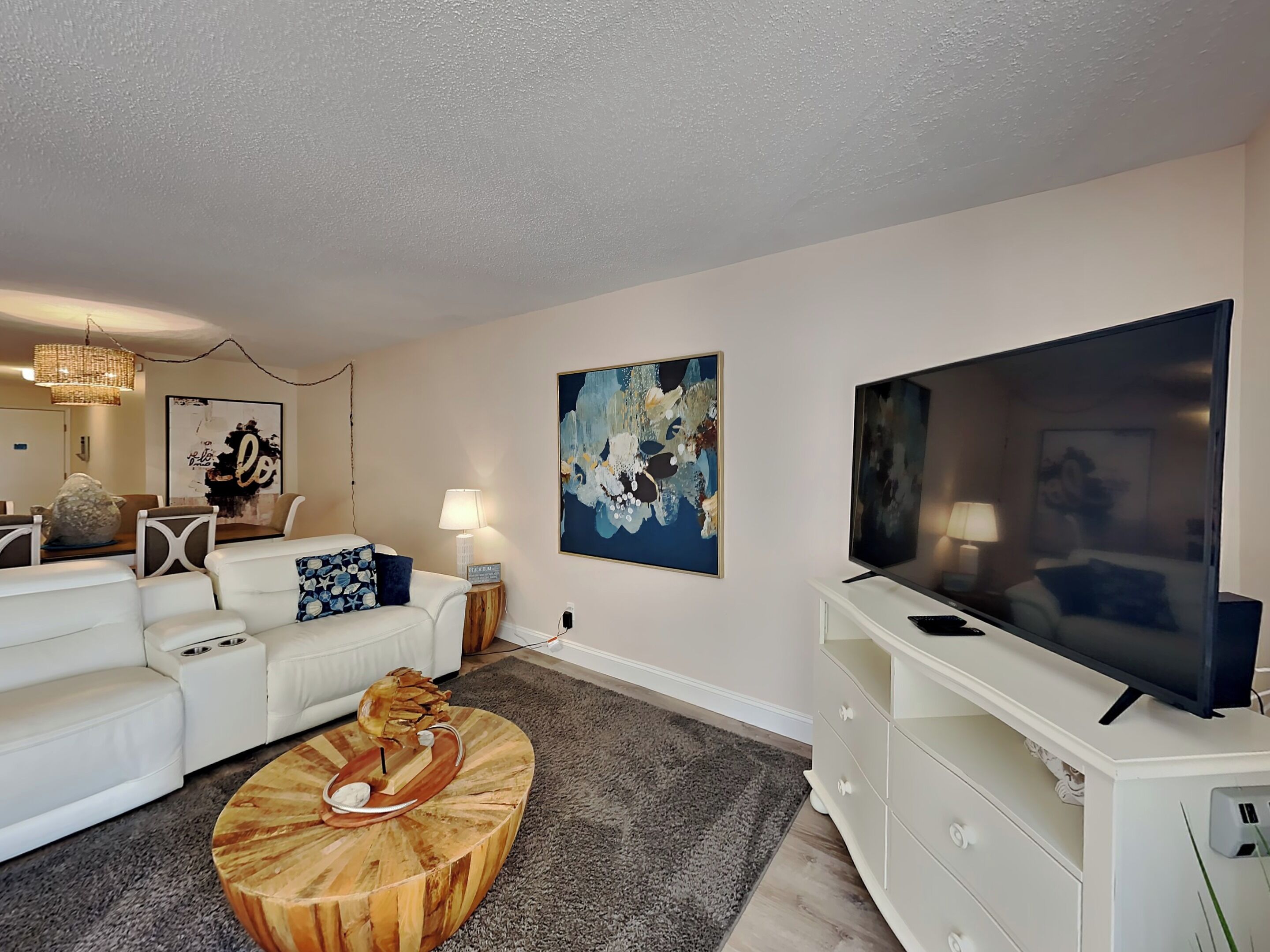 A modern living room with a white sofa, a round wooden coffee table, a flat-screen TV, and abstract wall art.