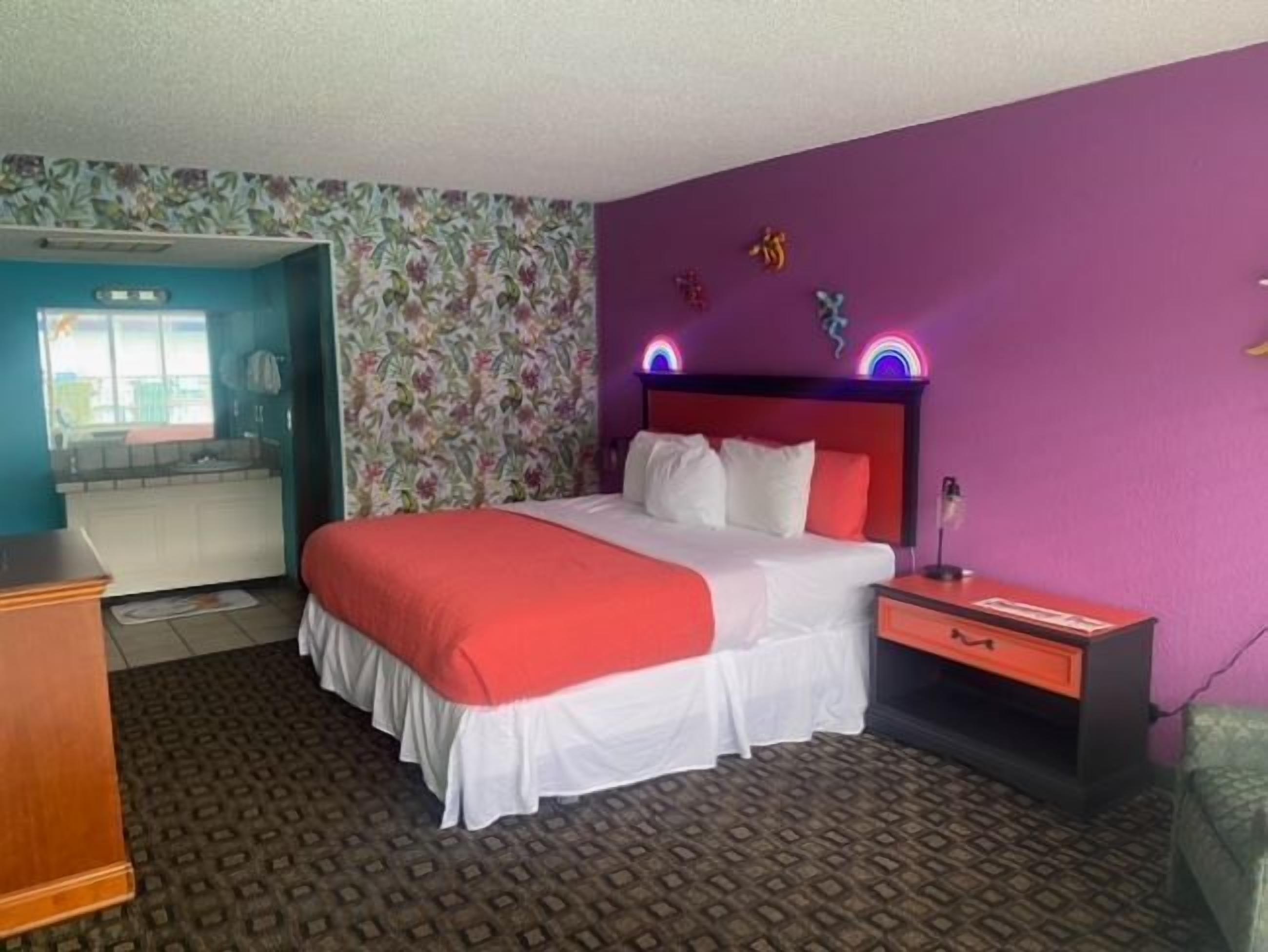 Une chambre d’hôtel avec un lit, une table de chevet, une commode et une salle de bain visible à travers une porte ouverte.