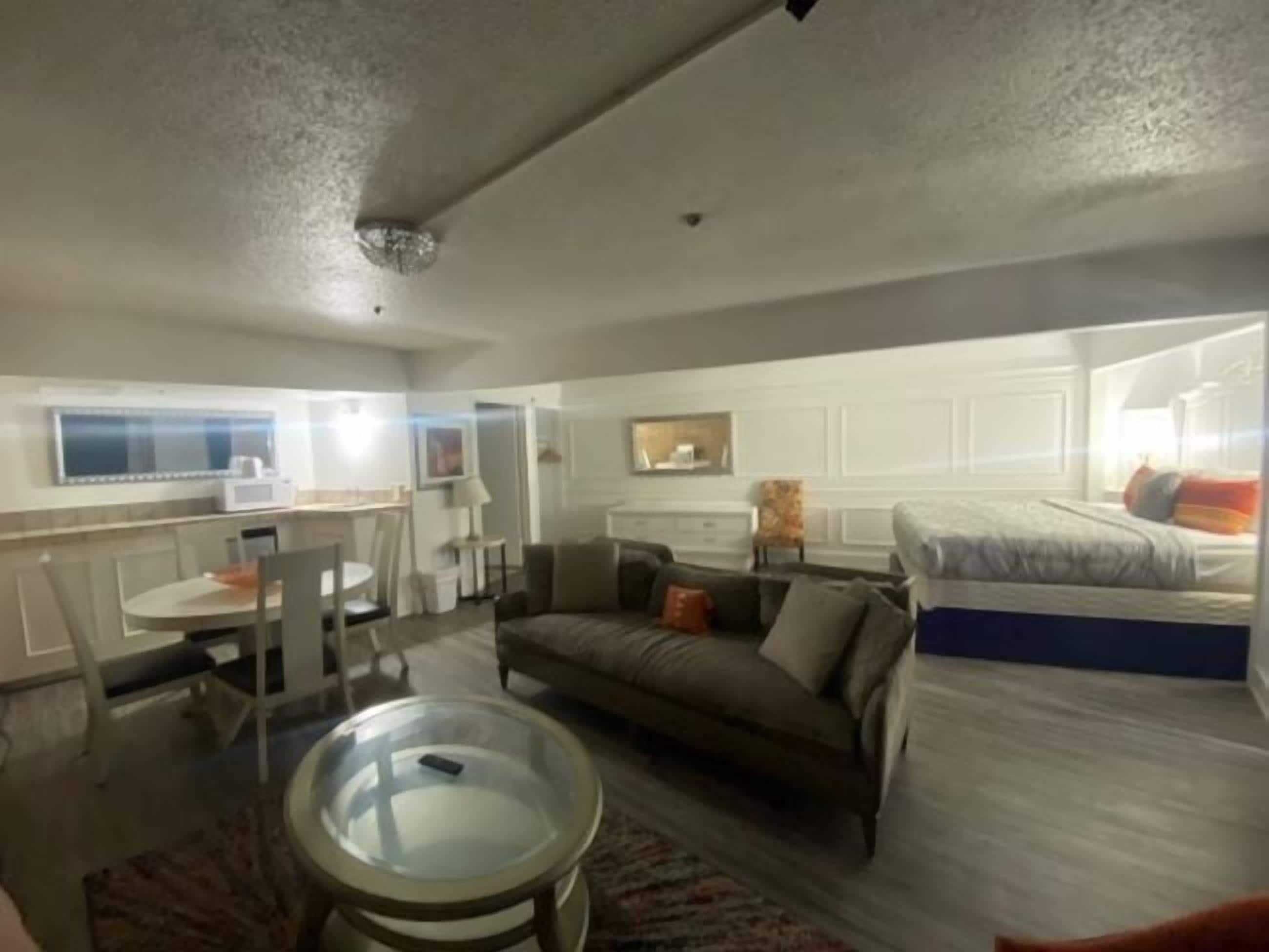 A compact hotel room with a kitchenette, a sofa, a bed, and a glass coffee table.