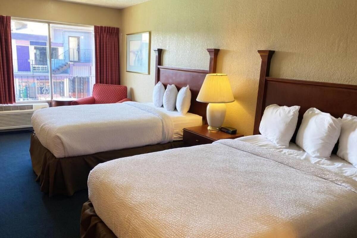 A hotel room with two beds, a window with curtains, a lamp, and a framed picture on the wall.