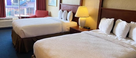 Ein Hotelzimmer mit zwei Betten, einem Fenster mit Vorhängen, einer Lampe und einem gerahmten Bild an der Wand.