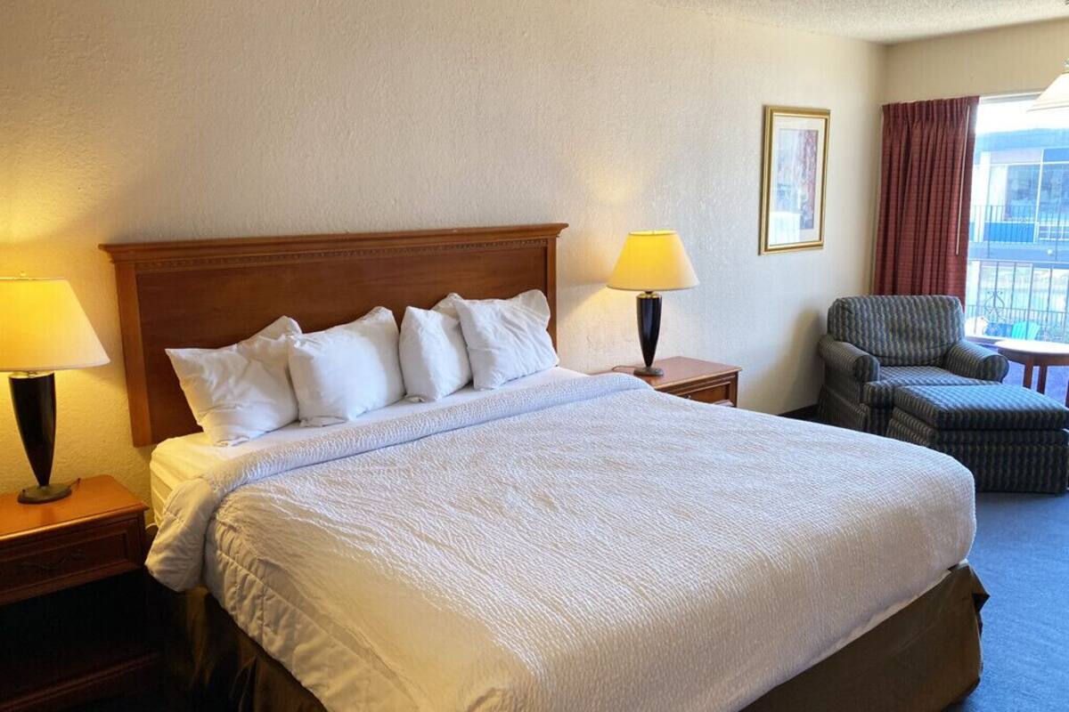 A hotel room with a large bed, two bedside tables with lamps, a chair, and a view of the outdoors.