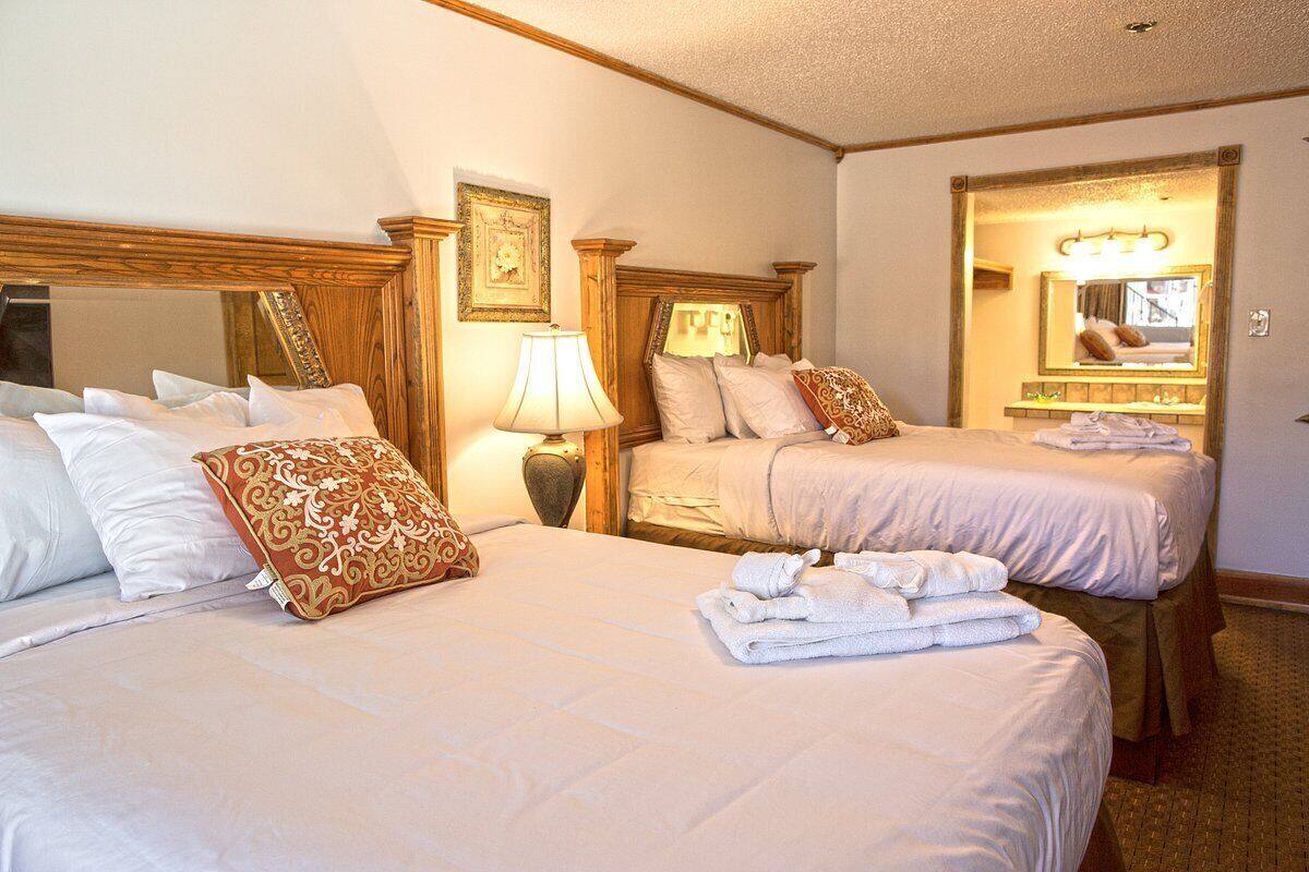 A hotel room with two beds, each with white linens and decorative pillows. There is a lamp on one side and a mirror on the opposite wall.
