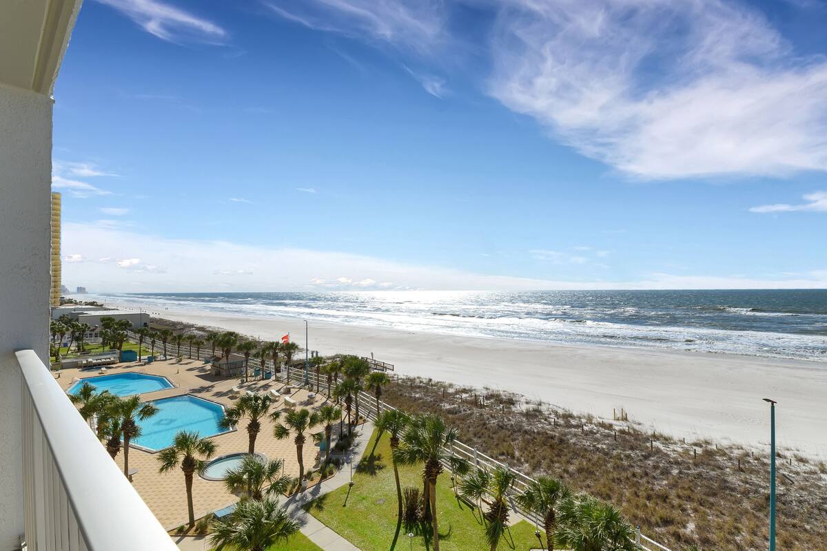 A beach view from a balcony with a pool and palm trees.