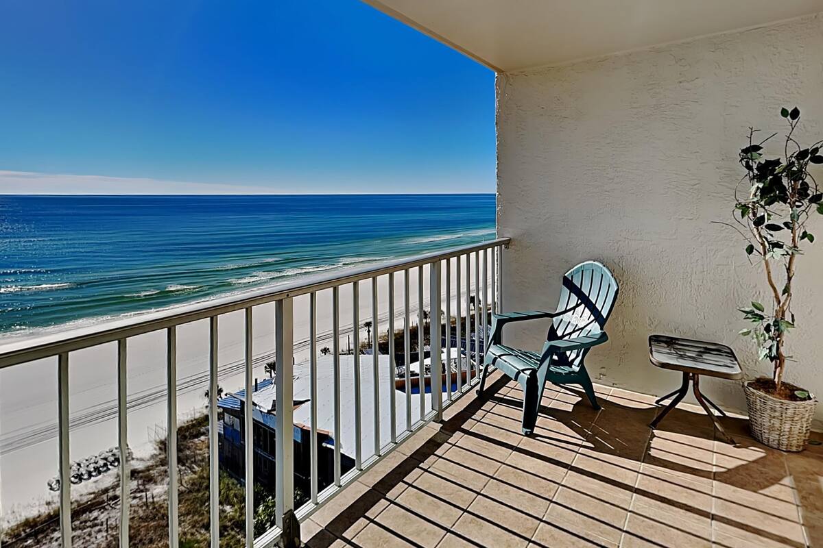 A balcony with a view of the ocean, a chair, a small table, and a potted plant.