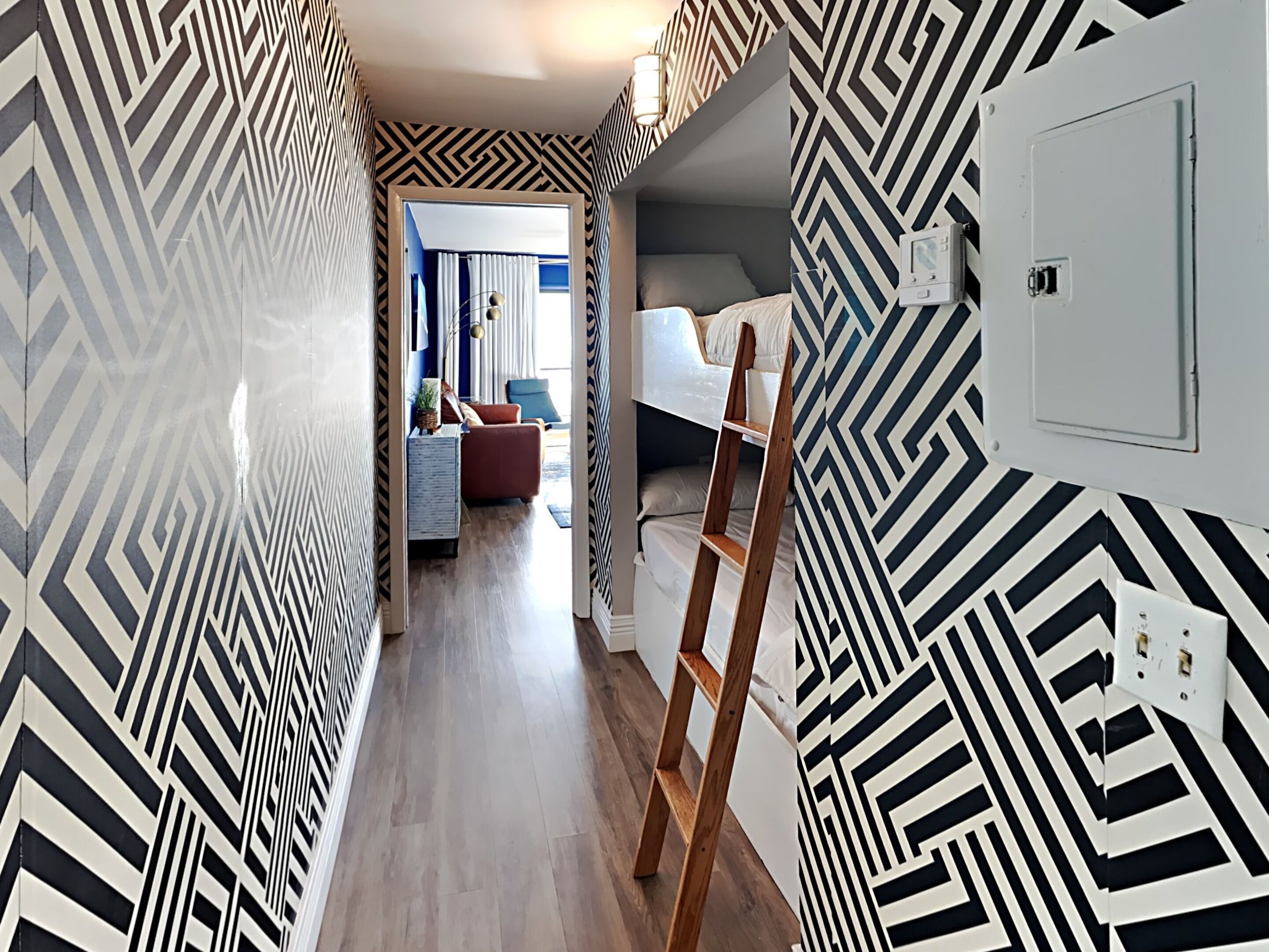 A hallway with geometric patterned walls, a wooden ladder, a bunk bed, and a small seating area with a red chair and a table.