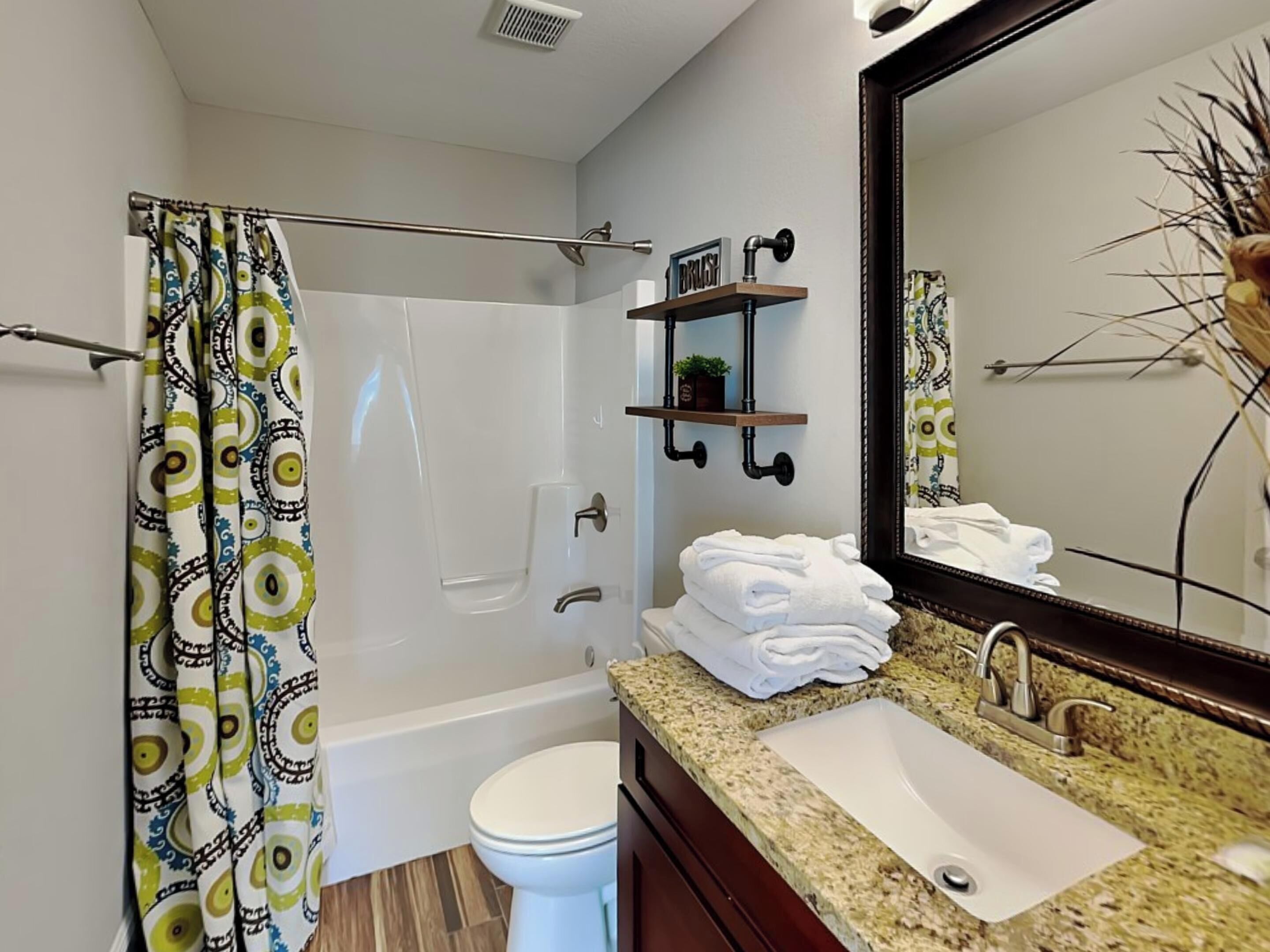 A bathroom with a shower, toilet, sink, and a mirror.