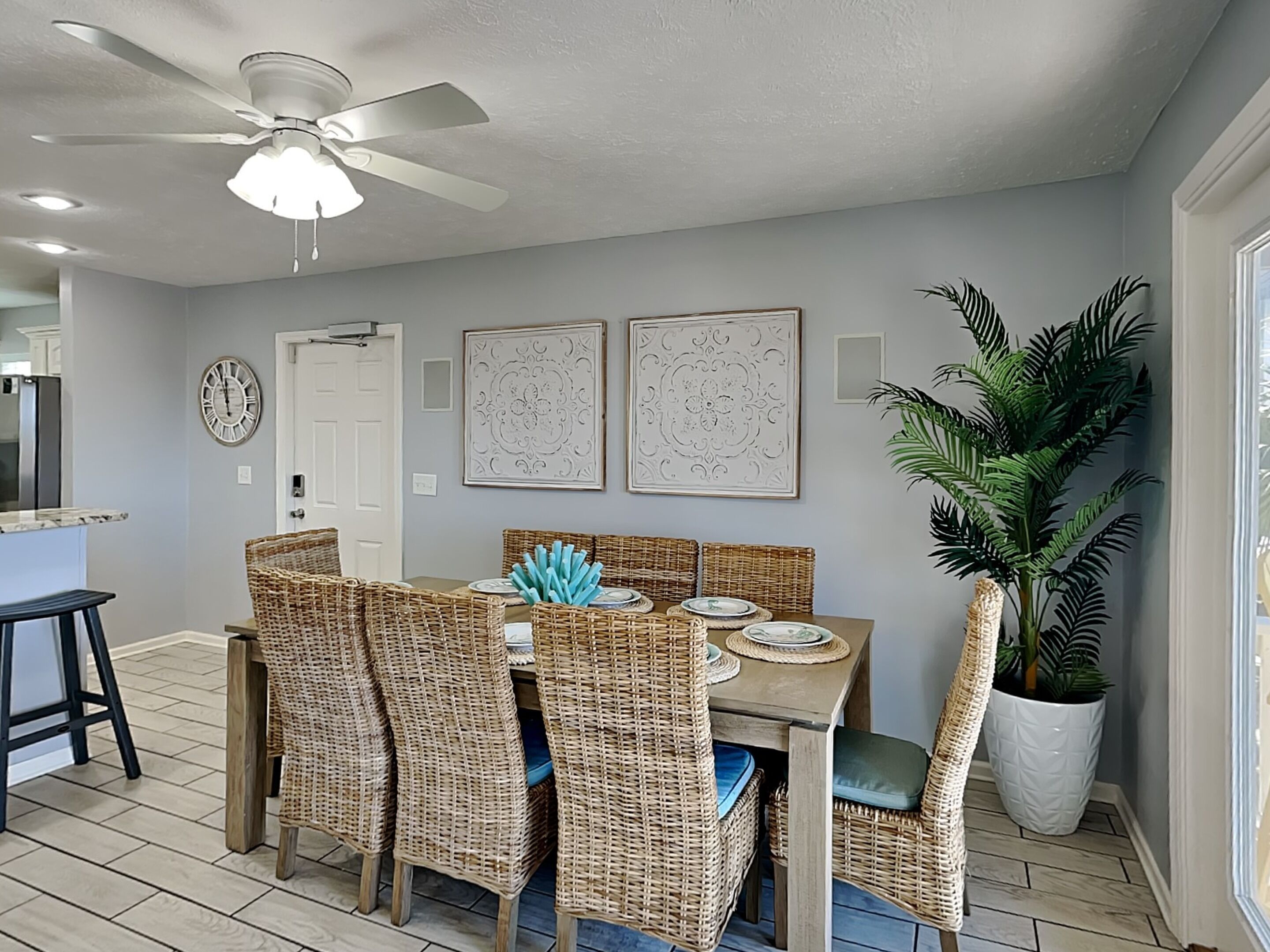 A dining area with a round table, wicker chairs, and a ceiling fan.