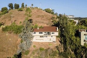 A two-story house with a flat roof, surrounded by trees and hills.