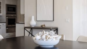 Ein Essbereich mit einer Pastaschale auf einem Tisch, einer weißen Vase und einem gerahmten Bild an der Wand.