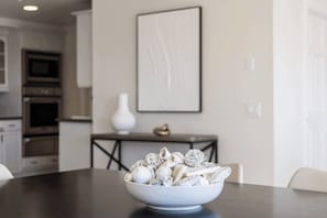 Uma área de refeições com um prato de massa sobre uma mesa, um vaso branco e um quadro na parede.