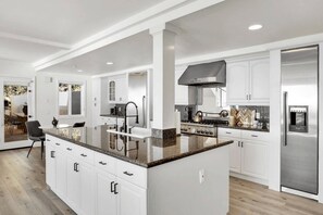 A modern kitchen with white cabinetry, a granite countertop, stainless steel appliances, and a central island.