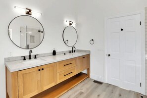 A modern bathroom with two sinks, wooden cabinets, and two round mirrors with lights.