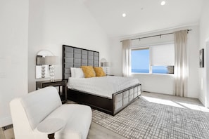 Quarto moderno com uma cama grande, uma poltrona, mesa de cabeceira e janela com vista.