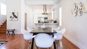 A modern kitchen with white cabinets, a central island, and a dining area with a black table and white chairs. - Ince by Avantstay 100 Meters to Amazon Studios (Culver City)