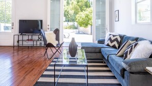 A modern living room with a sofa, a glass coffee table, a TV, and a view of a garden through glass doors. - Ince by Avantstay 100 Meters to Amazon Studios (Culver City)