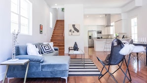 A modern living room with a blue sofa, a coffee table, and a black folding chair. A staircase leads to the kitchen in the background. - Ince by Avantstay 100 Meters to Amazon Studios (Culver City)