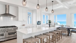 A modern kitchen with white cabinetry, a large island with bar stools, stainless steel appliances, and pendant lighting.