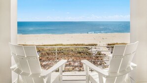A balcony with white chairs overlooking a beach.