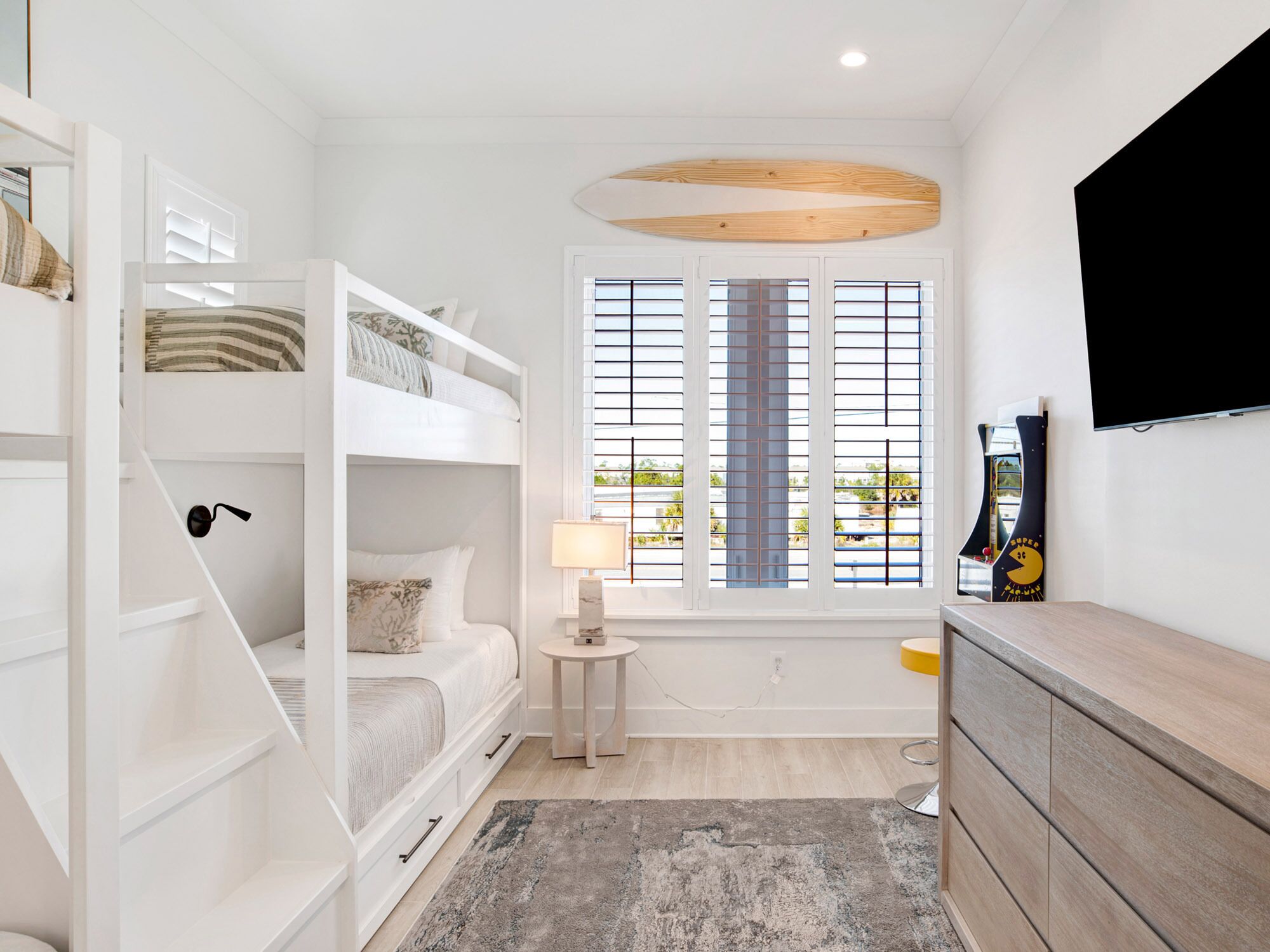A modern bedroom with bunk beds, a small bedside table, a lamp, a TV, and a window with blinds.
