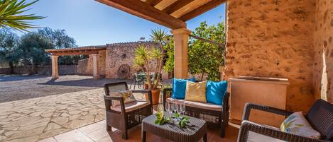 An outdoor patio with wicker furniture, a stone wall, and a pergola.