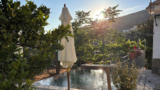 A poolside area with lounge chairs and a pergola, surrounded by greenery and a view of a hillside. - Finca Las Fuentezuelas (Carataunas)