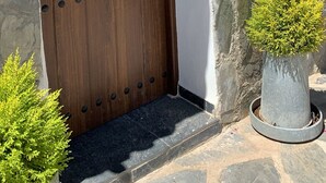 A wooden door with a metal handle, a white wall with a sign reading "CASA 1", and a stone wall with a potted plant. - Finca Las Fuentezuelas (Carataunas)