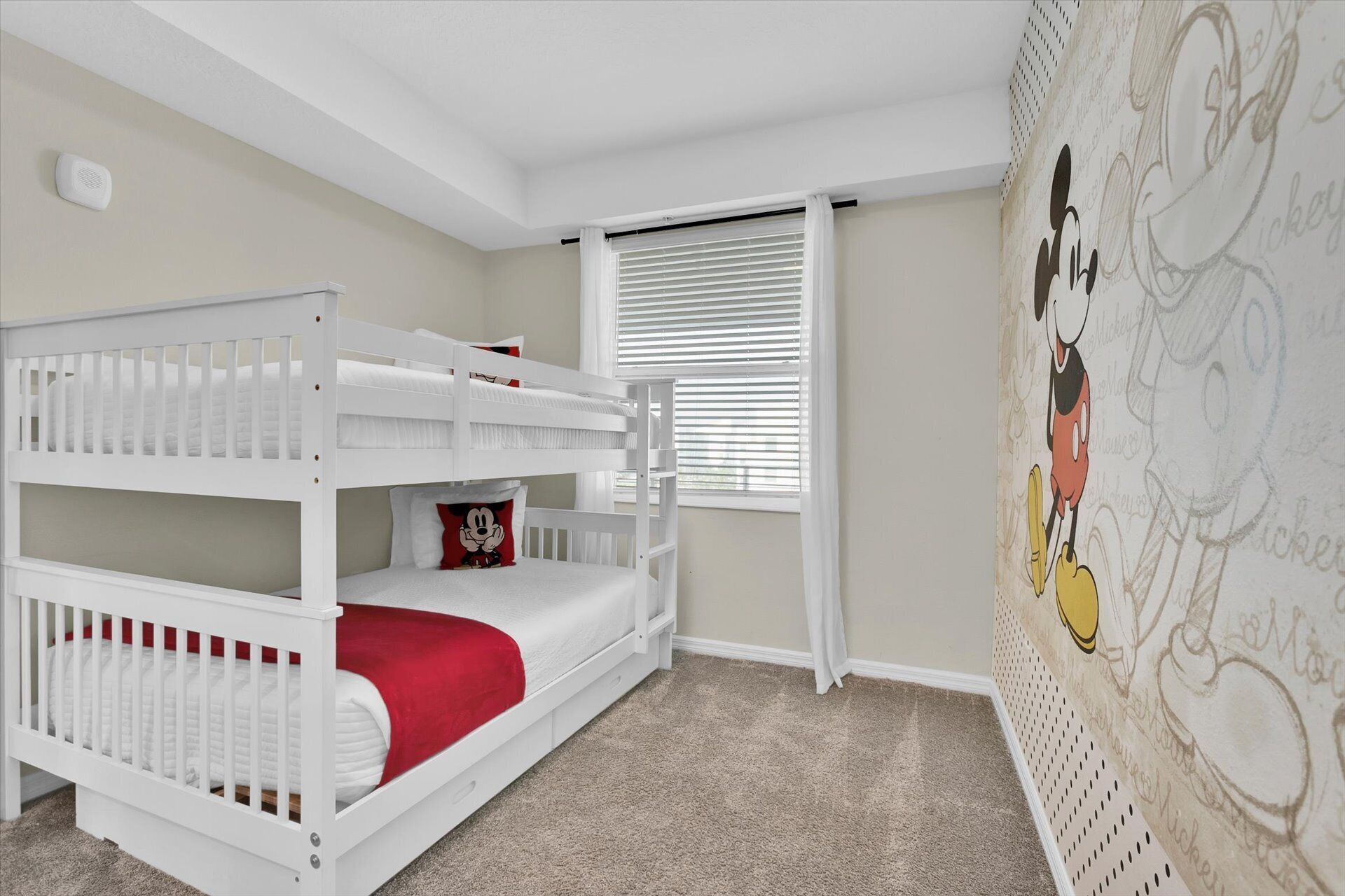 A child's room with a bunk bed, a window with blinds, and a Mickey Mouse mural on the wall.