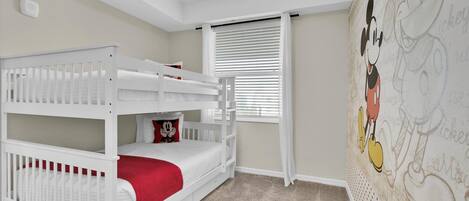 A child's room with a bunk bed, a window with blinds, and a Mickey Mouse mural on the wall.