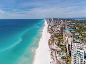 Un paisaje urbano costero con una extensa playa de arena, edificios altos y un cielo azul despejado.