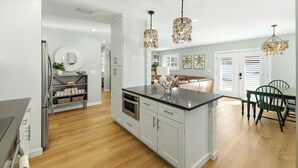 Une cuisine moderne avec des meubles blancs, un îlot central, des appareils en acier inoxydable et un coin repas avec une table et des chaises vertes.