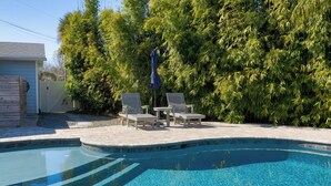 Une piscine bordée de deux chaises longues et d’une table, le tout entouré d’un luxuriant feuillage verdoyant.